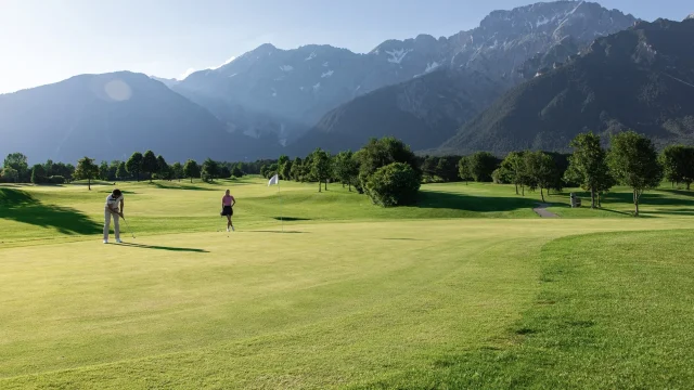 Golfspieler auf einem Platz mit Bergen im Hintergrund.