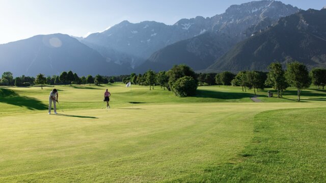 Golfspieler auf einem Platz mit Bergen im Hintergrund.