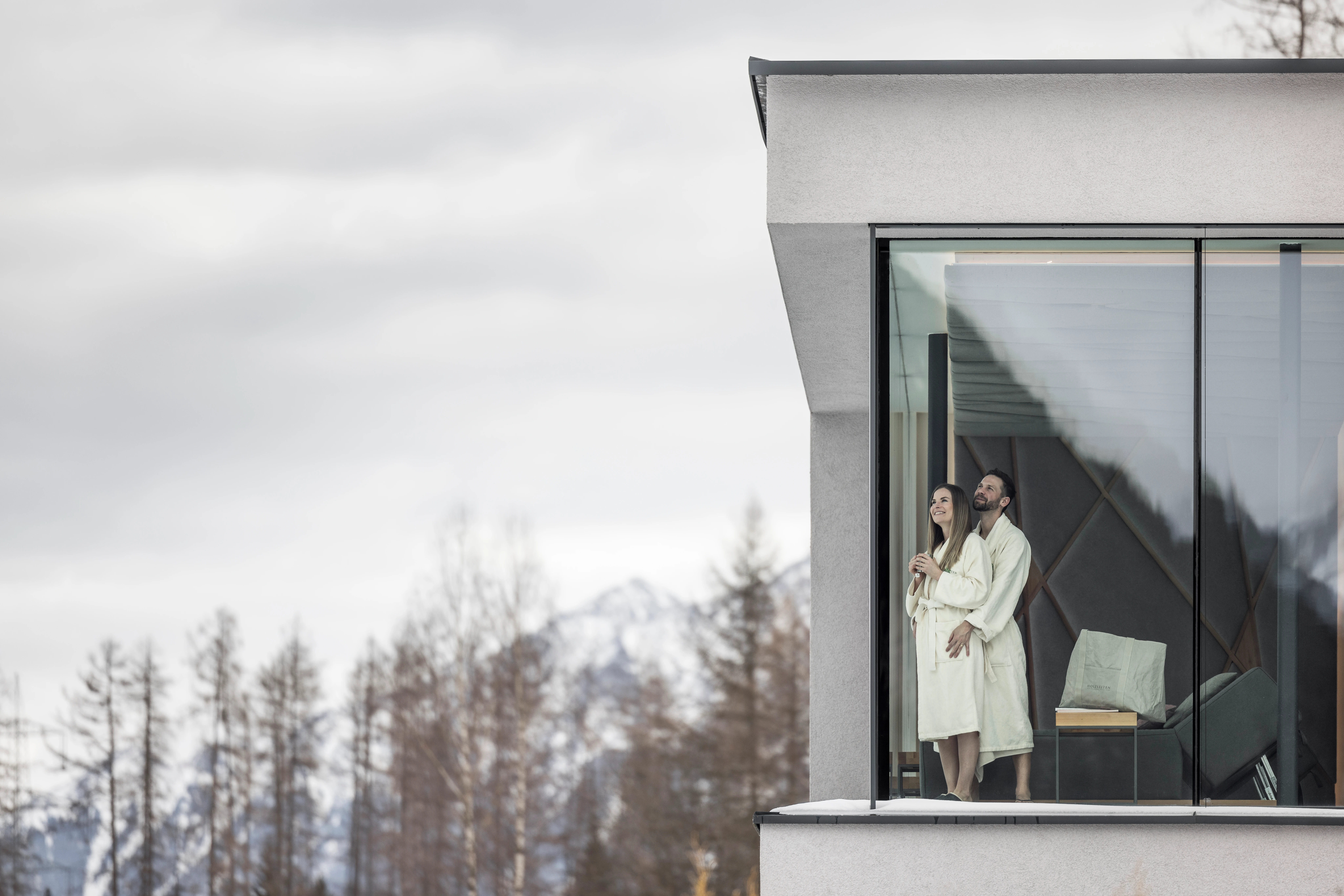 Paar in Bademänteln vor Fenster mit Bergblick