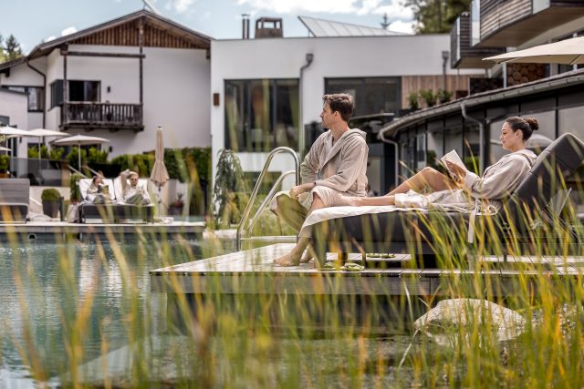 Paar entspannt am Pool eines luxuriösen Spa-Resorts in Bademänteln.