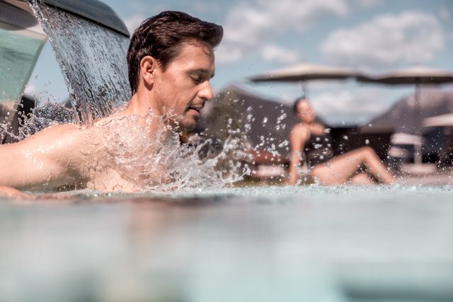 Mann unter einem Wasserfall im Pool, entspannter Urlaubstag.