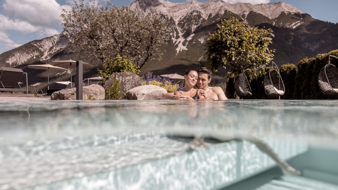 Ein Paar entspannt in einem Pool mit Bergblick und Hängekörben