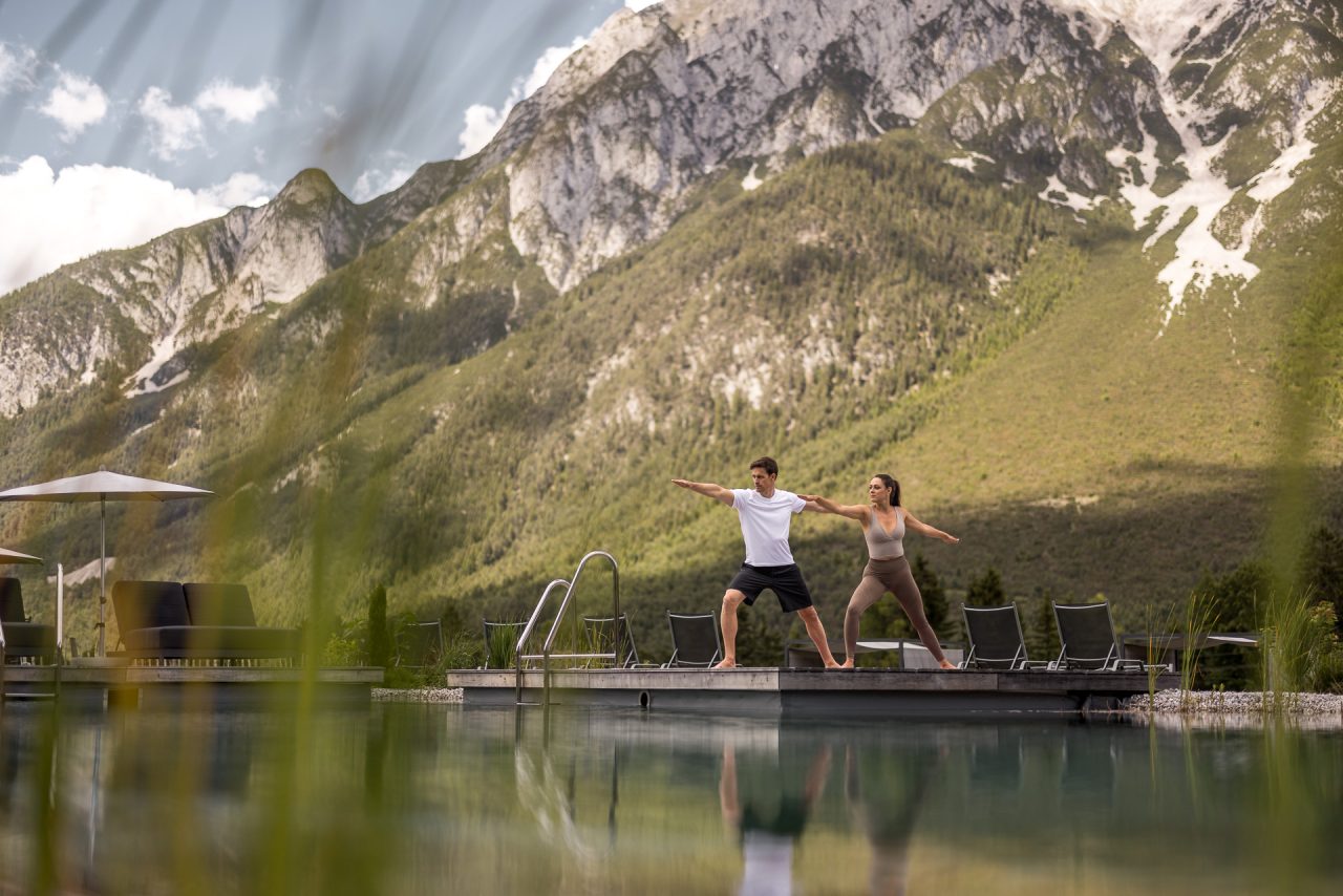 Paar macht Yoga an einem Pool mit Bergkulisse