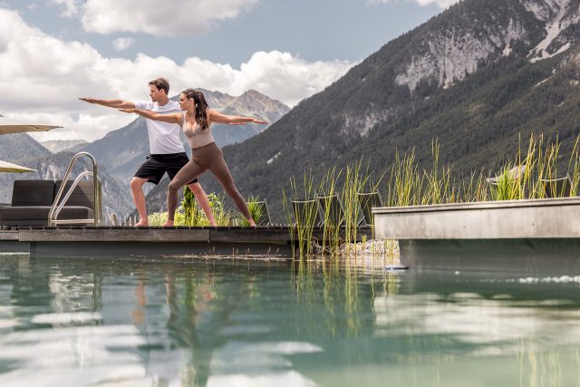 Paar macht Yoga im Freien am Pool mit Bergkulisse