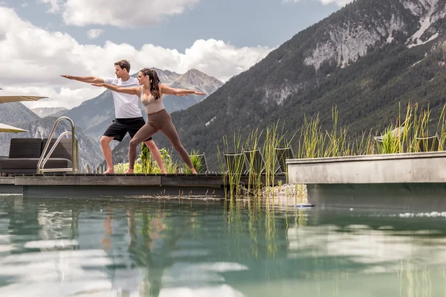 Paar macht Yoga im Freien am Pool mit Bergkulisse